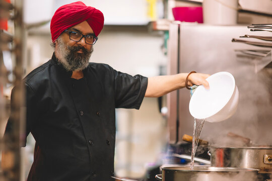 Chef in traditional turban cooking in commercial kitchen