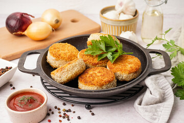 Frying pan with tasty meat cutlets and sauce on white background