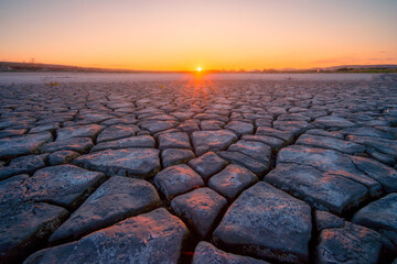 The golden sunset casts a warm glow over a vast landscape of textured mudcracks, symbolizing drought and the beauty of natural patterns