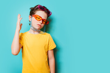 Young child with layered sunglasses posing on teal background