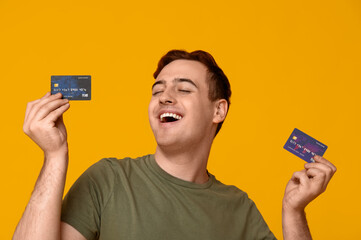 Young man with credit cards on yellow background