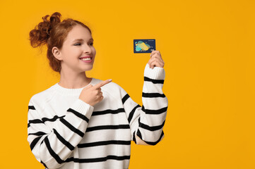 Beautiful young woman pointing at credit card on yellow background