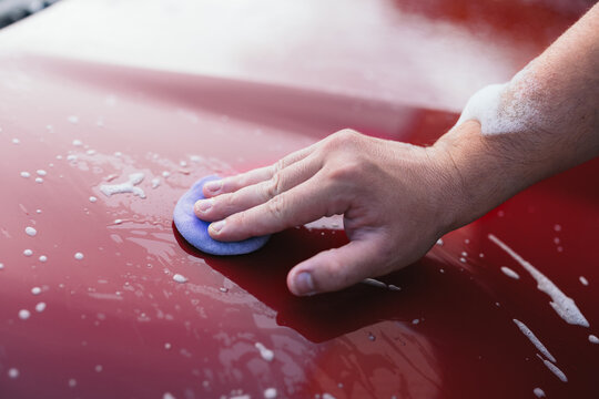 Hand polishing a red car with foam pad and soap suds