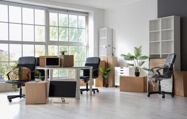 Interior of modern office with chairs, houseplants and cardboard boxes on moving day