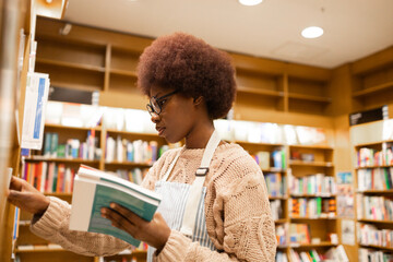 Young African American woman browsing books in a library aisle