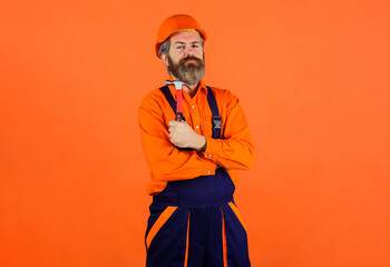 Builder in construction overalls and hard hat with hammer. Bearded man in builders uniform and...