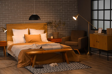 Interior of bedroom with glowing lamps, armchair and wooden bench at night