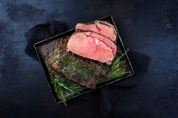 Traditional Commonwealth Sunday roast beef sliced with herbs served as top view on a rustic black...