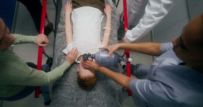 Medical staff and parents carry the boy on a gurney, giving him oxygen with a mask, top view
