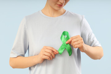 Young woman with green ribbon on light background, closeup. Glaucoma awareness month