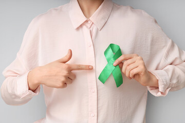 Young businesswoman pointing at green ribbon on light background, closeup. Glaucoma awareness month