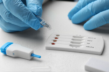 Doctor dropping buffer solution onto disposable multi-infection express test cassette at white table, closeup