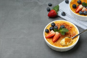 Delicious creme brulee with berries in bowl and spoon on grey table. Space for text