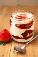 Tasty yoghurt with jam, spoon and strawberry on wooden table, closeup