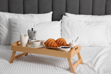 Wooden tray with tasty breakfast on bed at home