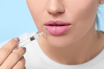 Beautiful young woman holding syringe with filler on color background, closeup