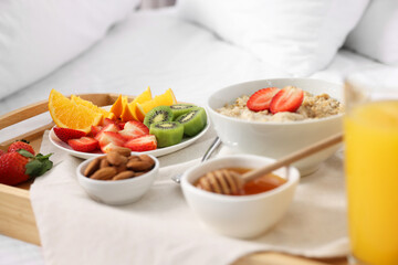 Tasty breakfast served in bed. Oatmeal, juice, fruits, almonds and honey on tray, closeup
