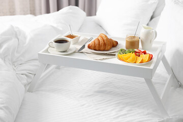 Wooden tray with tasty breakfast on bed at home