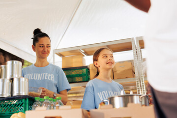 Caucasian mother and daughter volunteering at food drive, providing free food to the poor and...