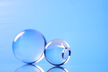 Transparent glass balls on mirror surface against blue background. Space for text
