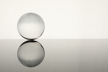Transparent glass ball on mirror surface against light background. Space for text