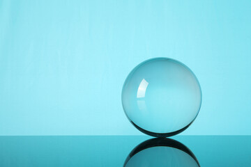 Transparent glass ball on mirror surface against turquoise background. Space for text