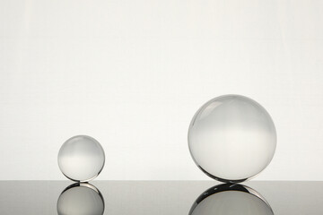 Transparent glass balls on mirror surface against light background. Space for text