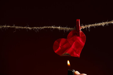 Lighting red paper heart with lighter on rope against burgundy background, space for text. Broken...