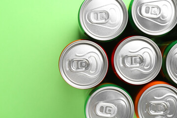 Energy drink in cans on light green background, top view. Space for text