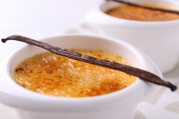 Delicious creme brulee in bowl and vanilla pod on table, closeup