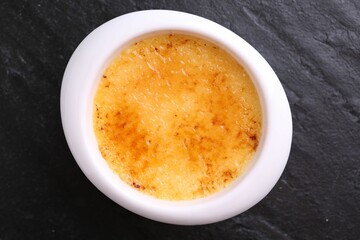 Delicious creme brulee in bowl on dark gray textured table, top view