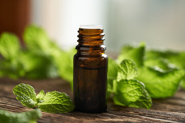 A brown bottle of aromatherapy essential oil with fresh peppermint leaves