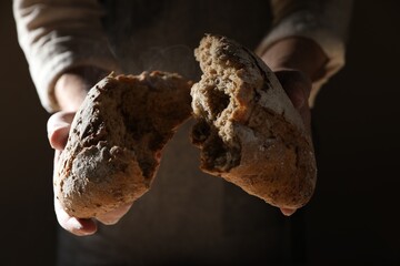 Man breaking loaf of fresh bread on dark background, closeup