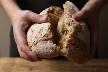 Man breaking loaf of fresh bread at wooden table, closeup