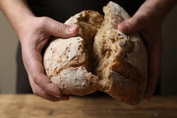 Gordijnen Man breaking loaf of fresh bread at wooden table, closeup © New Africa