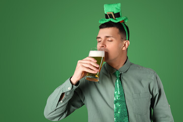 Young man drinking beer on green background. St. Patrick's Day