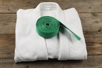 Green karate belt and white kimono on wooden background