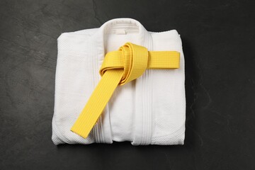 Yellow karate belt and white kimono on gray background, top view