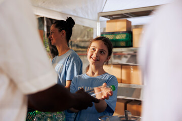 Cheerful caucasian girl volunteering by handing out free food to the needy at a non-profit food...