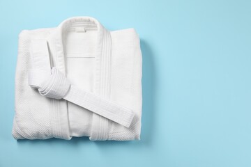 White karate belt and kimono on light blue background, top view. Space for text