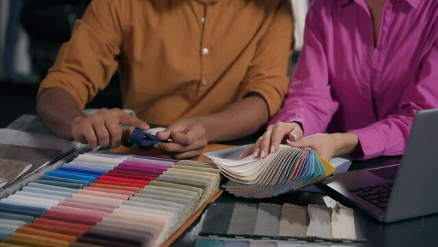 Unrecognizable woman man fashion designers choosing buying textile in atelier select materials cropped shot customers hands apply fabric sample choose color tone match with palette colors cloth design