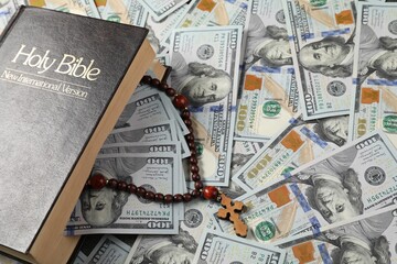Holy Bible and wooden cross on dollar banknotes, closeup