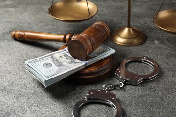 Judge's gavel, money, handcuffs and scales of justice on grey table