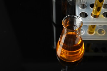 Laboratory glassware with different types of oil on black background, closeup. Space for text