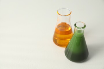 Glass flasks with different types of oil on white table, space for text