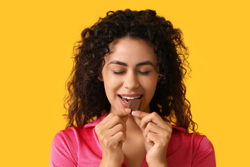 Beautiful young African-American woman eating piece of sweet chocolate on yellow background
