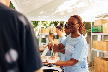 African american woman serving free food to the poor, needy individual at an outdoor food bank....