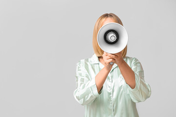 Mature woman in pajamas with megaphone on grey background