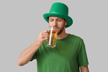 Young man in leprechaun hat drinking beer on grey background. St. Patrick's Day celebration