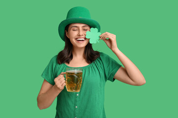 Happy young woman in leprechaun hat with glass of beer and clover on green background. St....